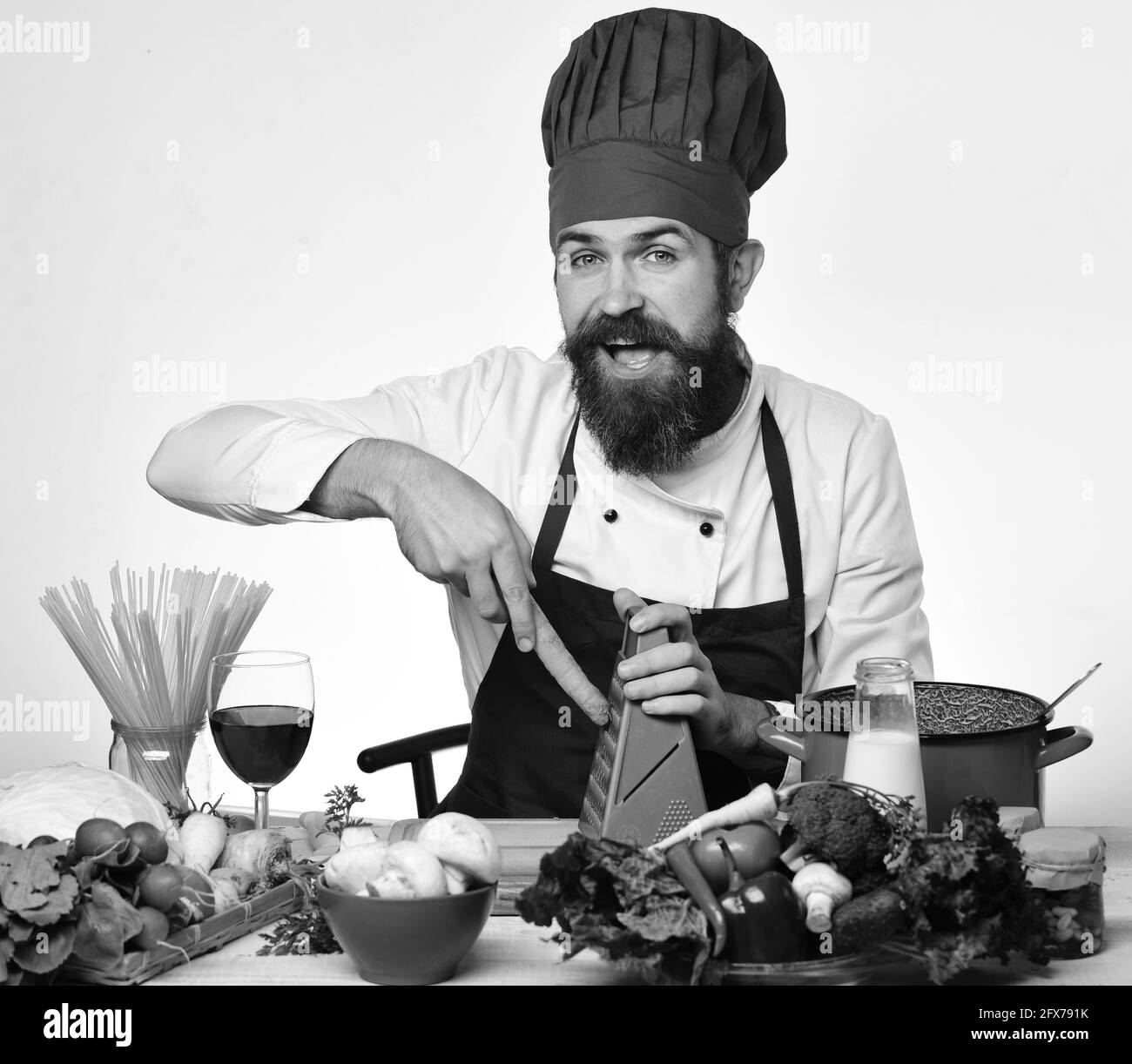 Cuisinez avec un visage curieux assis près d'une table de cuisine avec des légumes Banque D'Images