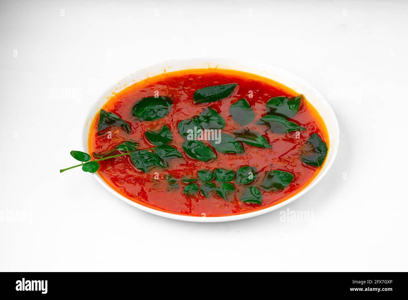 Sauce au curry de poisson rouge, disposée dans un bol blanc et garnie de feuilles de curry vertes fraîches sur fond blanc. Banque D'Images