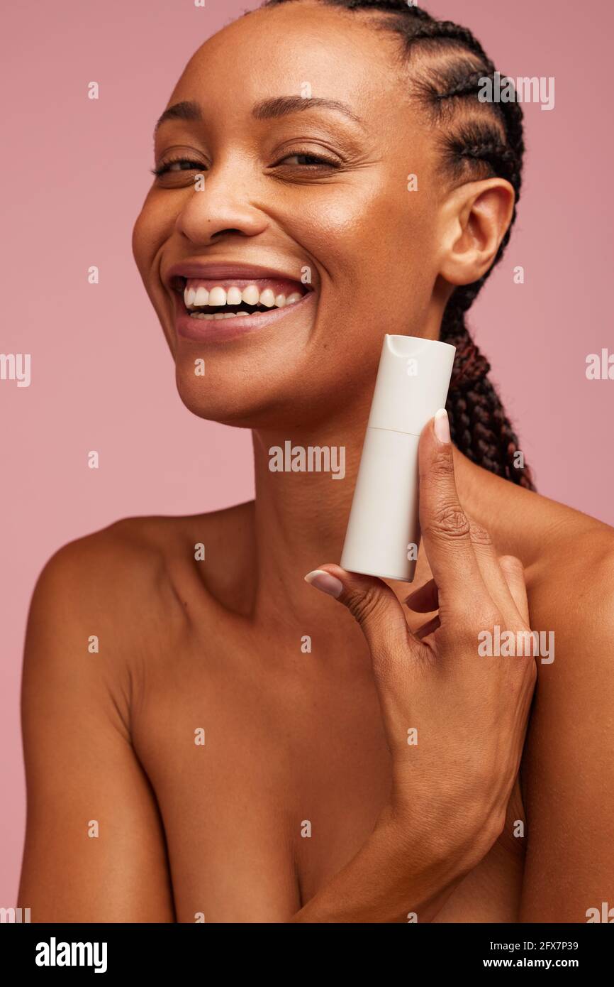 Femme souriante présentant un produit de beauté. Modèle féminin montrant un produit cosmétique pour une peau éclatante. Banque D'Images
