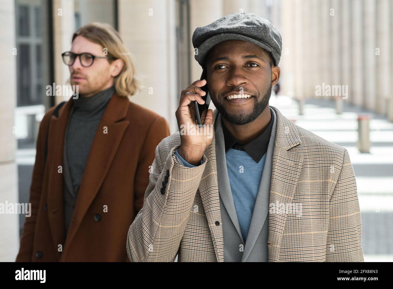 Homme d'affaires souriant africain parlant sur téléphone portable tout en marchant le long la rue Banque D'Images