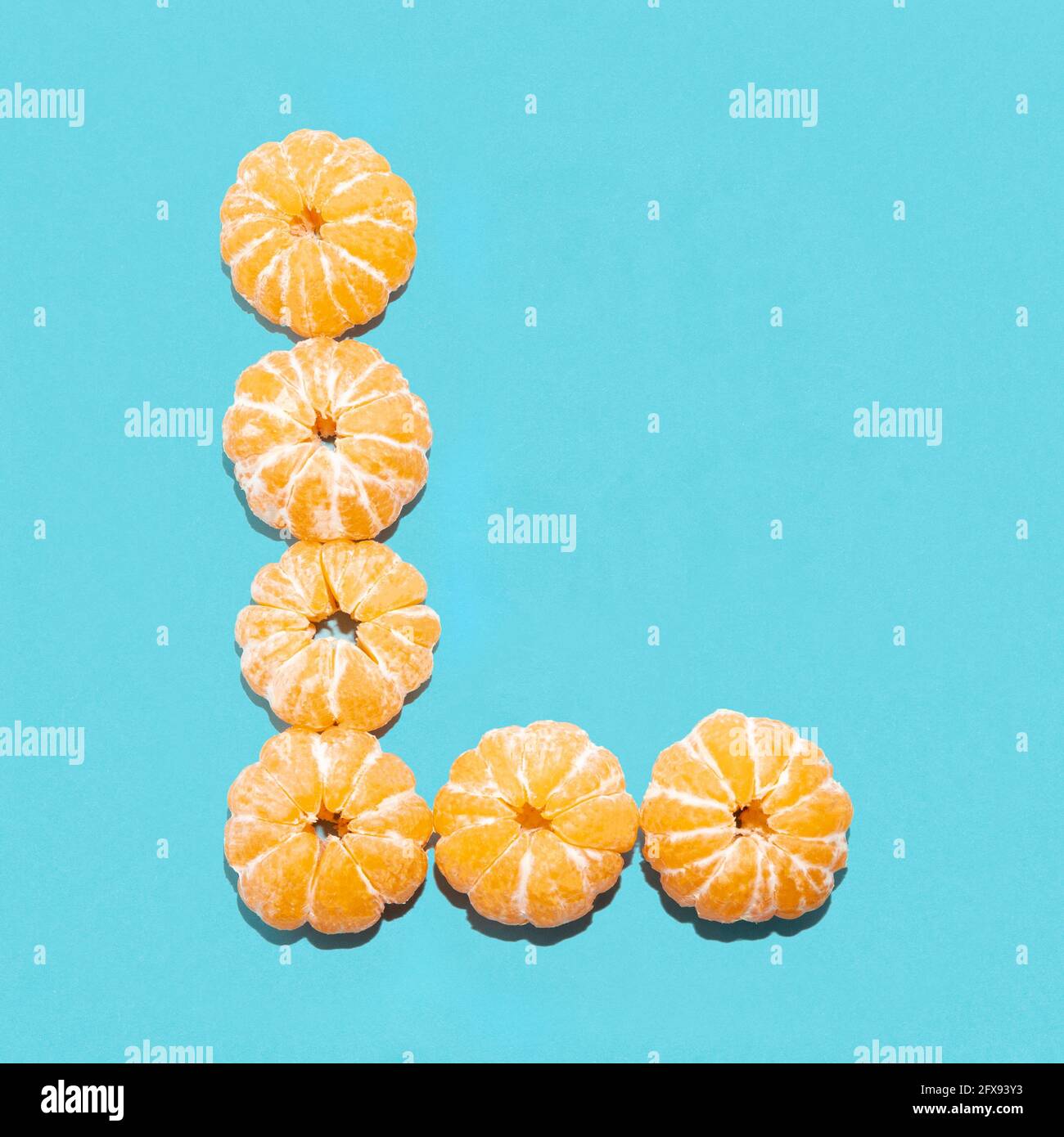 Mise en page créative de la lettre L de mandarines pelées sur fond bleu. Mise à plat. Banque D'Images