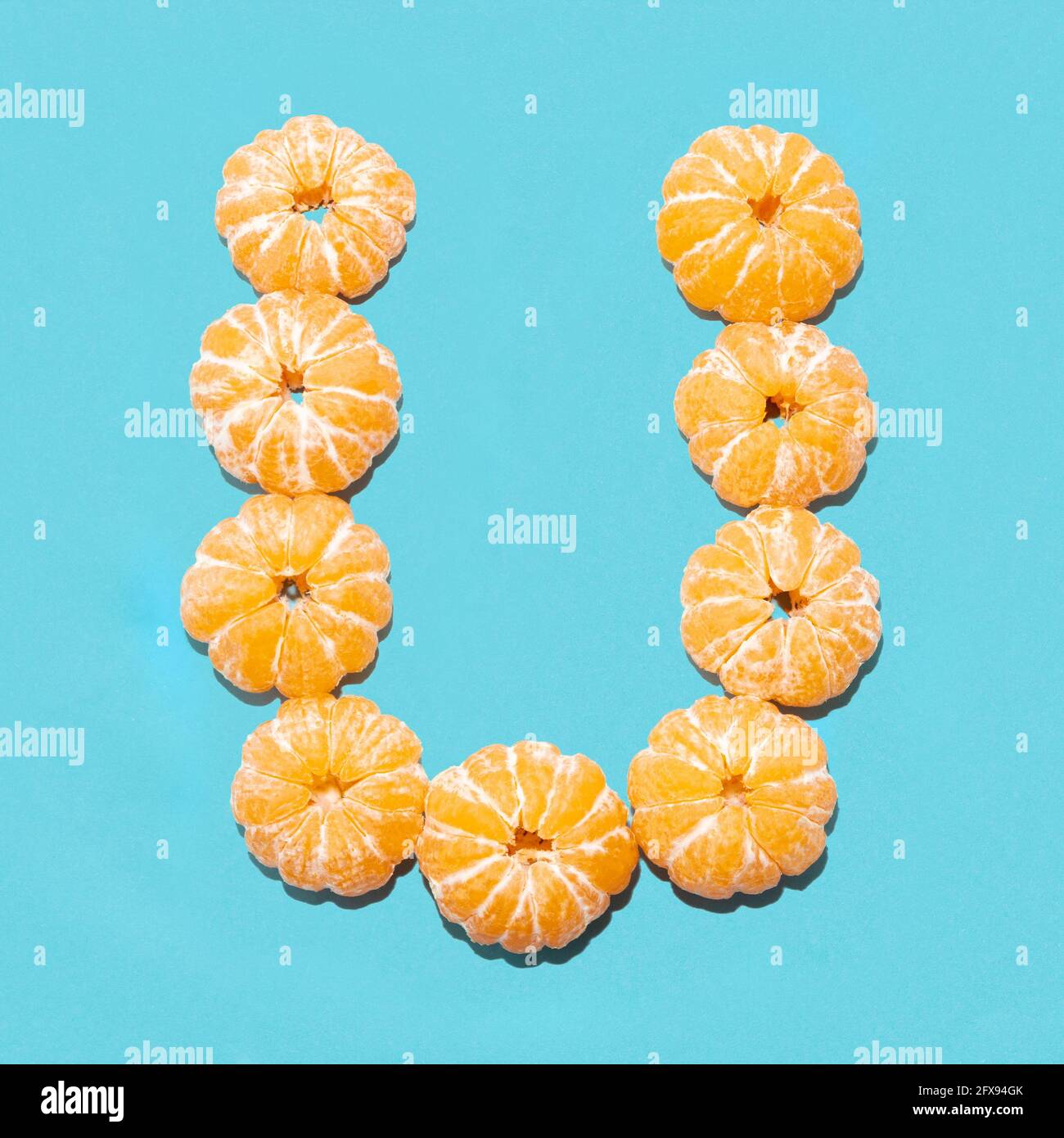 Mise en page créative de la lettre U de tangerines pelées sur fond bleu. Mise à plat. Banque D'Images