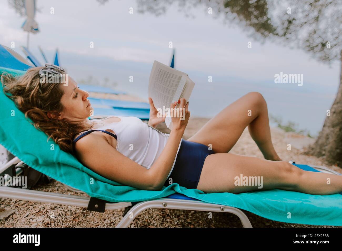 Une femme se bronzer et lire à la plage au bord de l'océan Banque D'Images