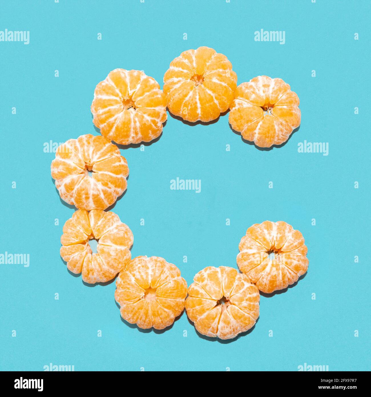 Mise en page créative de la lettre C de mandarines pelées sur fond bleu. Mise à plat. Banque D'Images