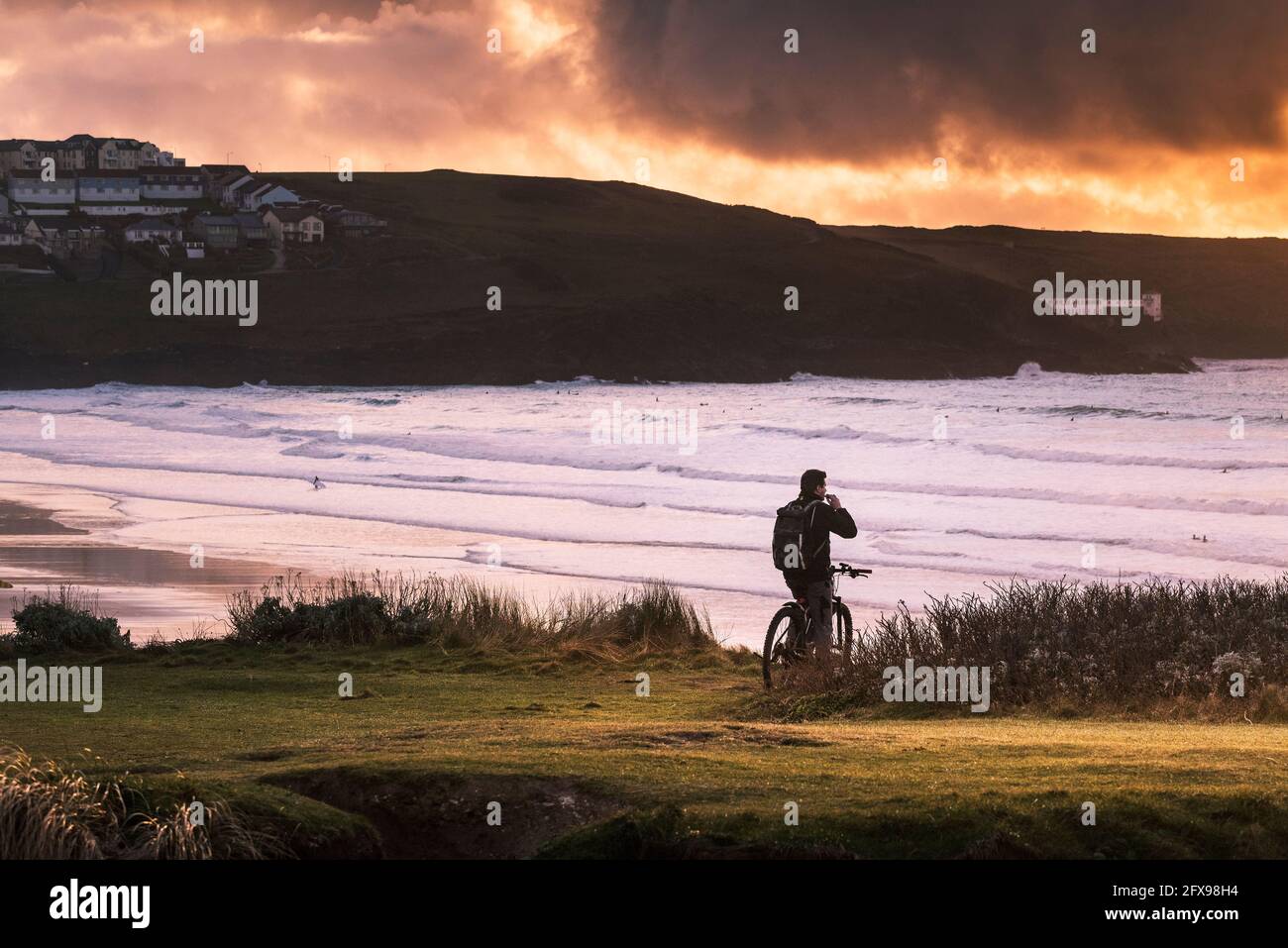 Cycliste debout sur le promontoire surplombant la baie de Fistral au coucher du soleil à Newquay, en Cornouailles. Banque D'Images