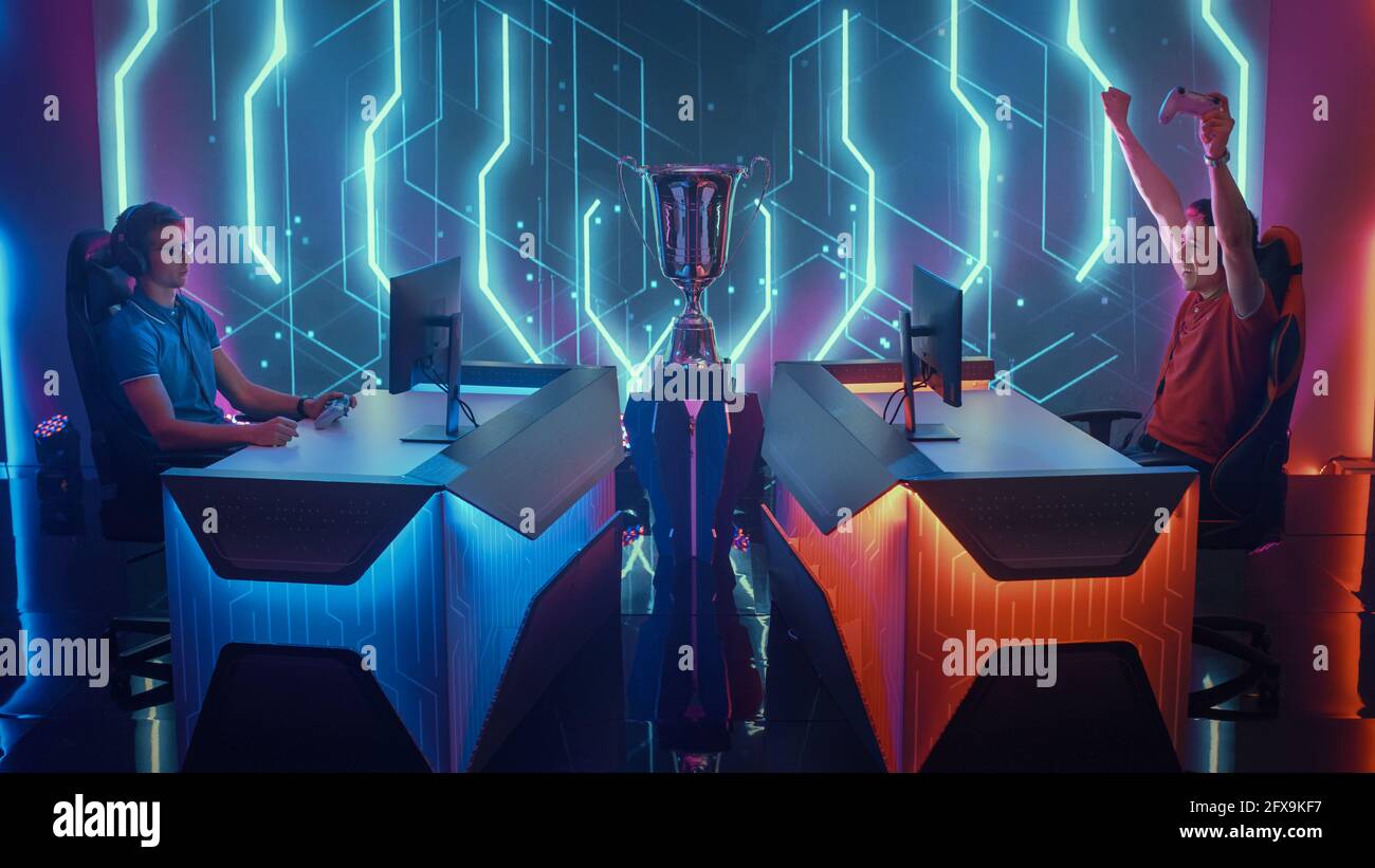 Deux gamers professionnels Esport utilisant des contrôleurs jouant à des jeux vidéo de console lors d'un événement de championnat, un joueur célèbre la victoire avec les mains levées Banque D'Images