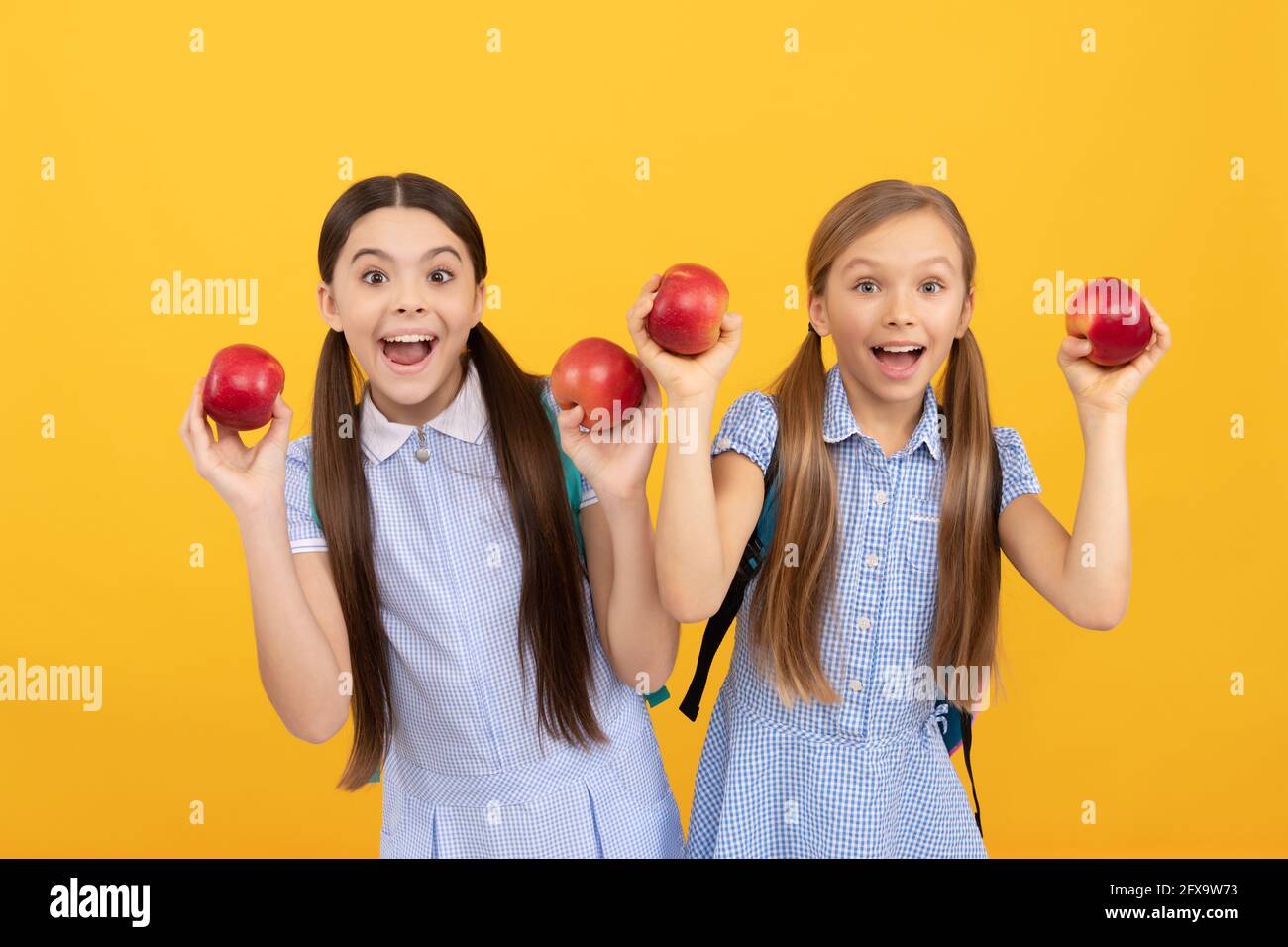 Les enfants heureux tiennent des pommes pour une collation saine de retour à l'école fond jaune, l'alimentation scolaire Banque D'Images