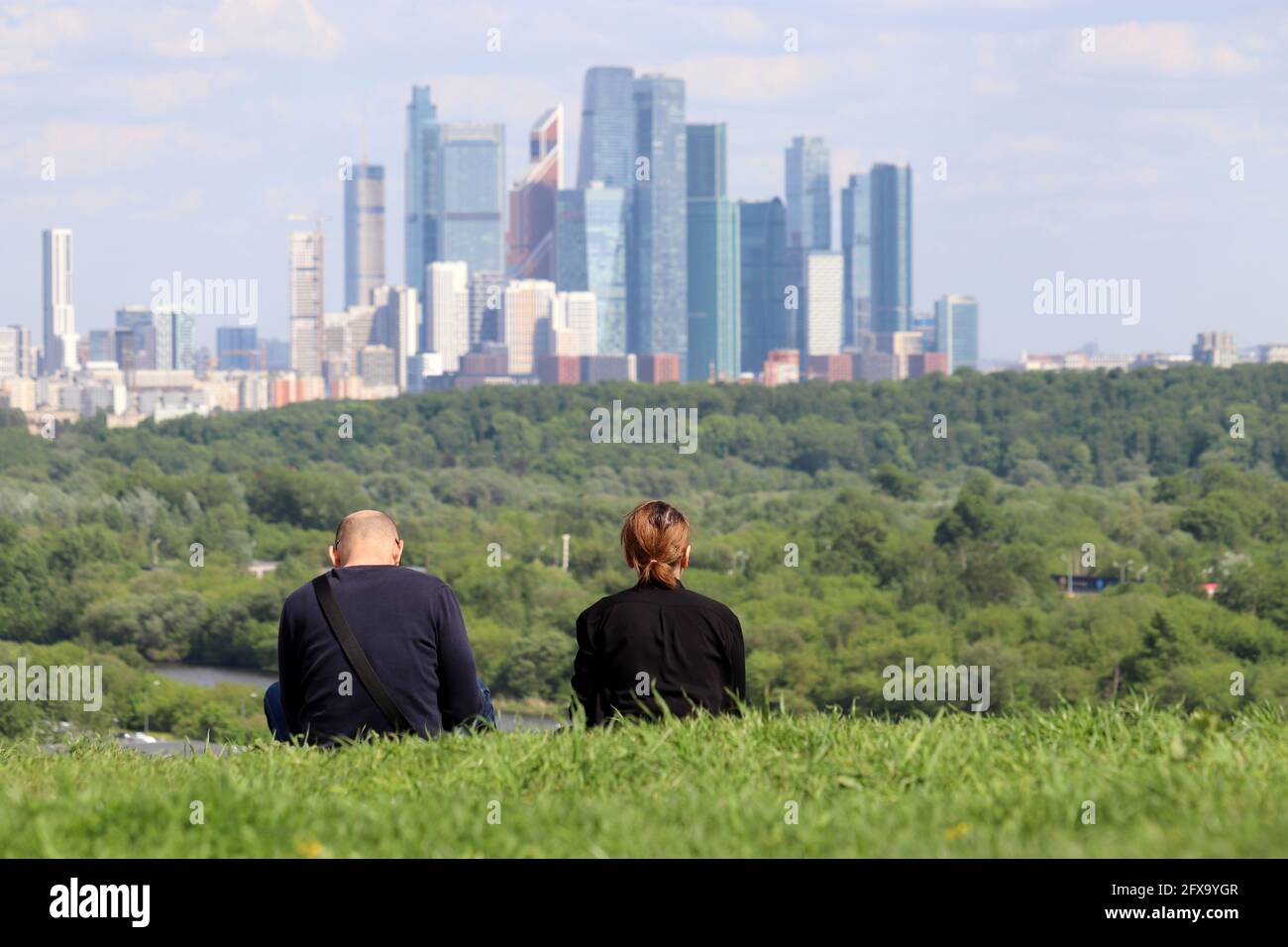 Couple assis dans l'herbe contre les gratte-ciel de la ville de Moscou. Paysage urbain futuriste, concept de loisirs d'été suburbains Banque D'Images
