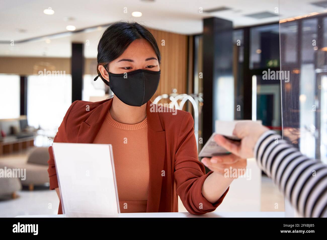 Une jeune femme sous masque prend la clé de la réceptionniste de l'hôtel Banque D'Images