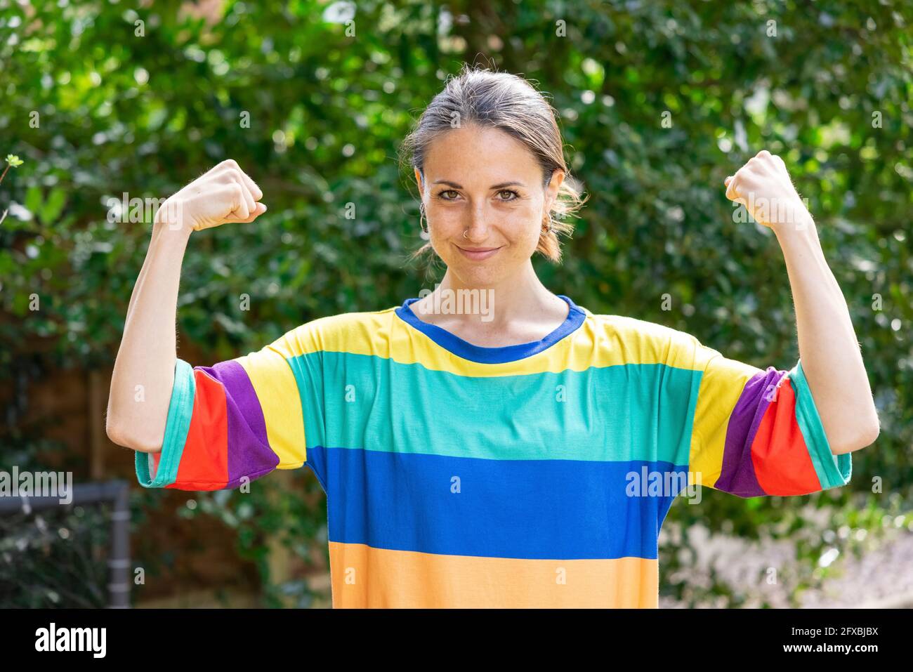 Belle femme adulte de taille moyenne portant des biceps flexibles multicolores dans le jardin Banque D'Images