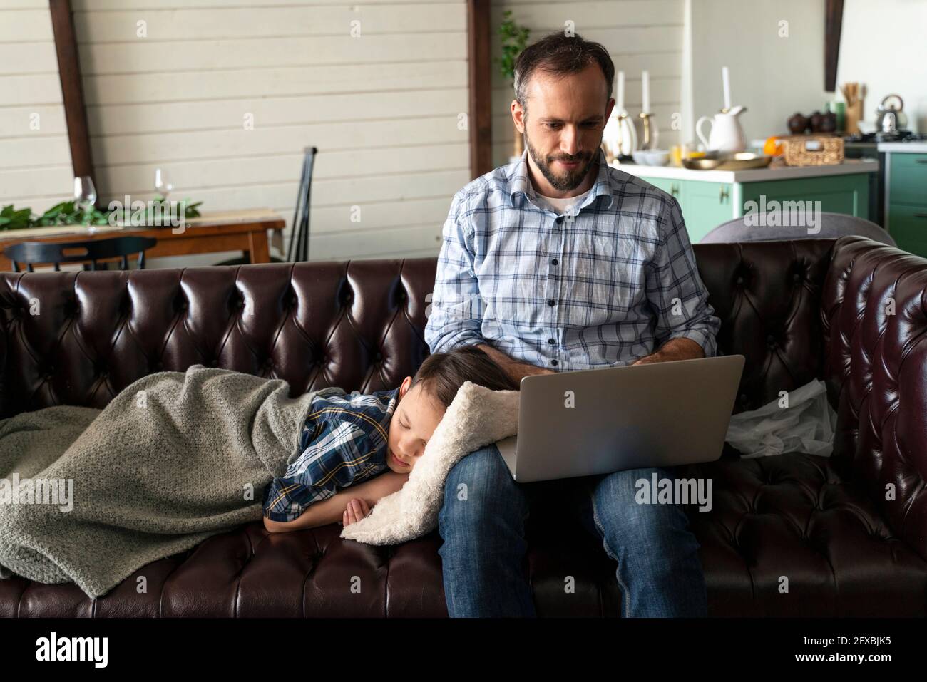 Fils dormant par le père en utilisant un ordinateur portable sur le canapé à la maison Banque D'Images