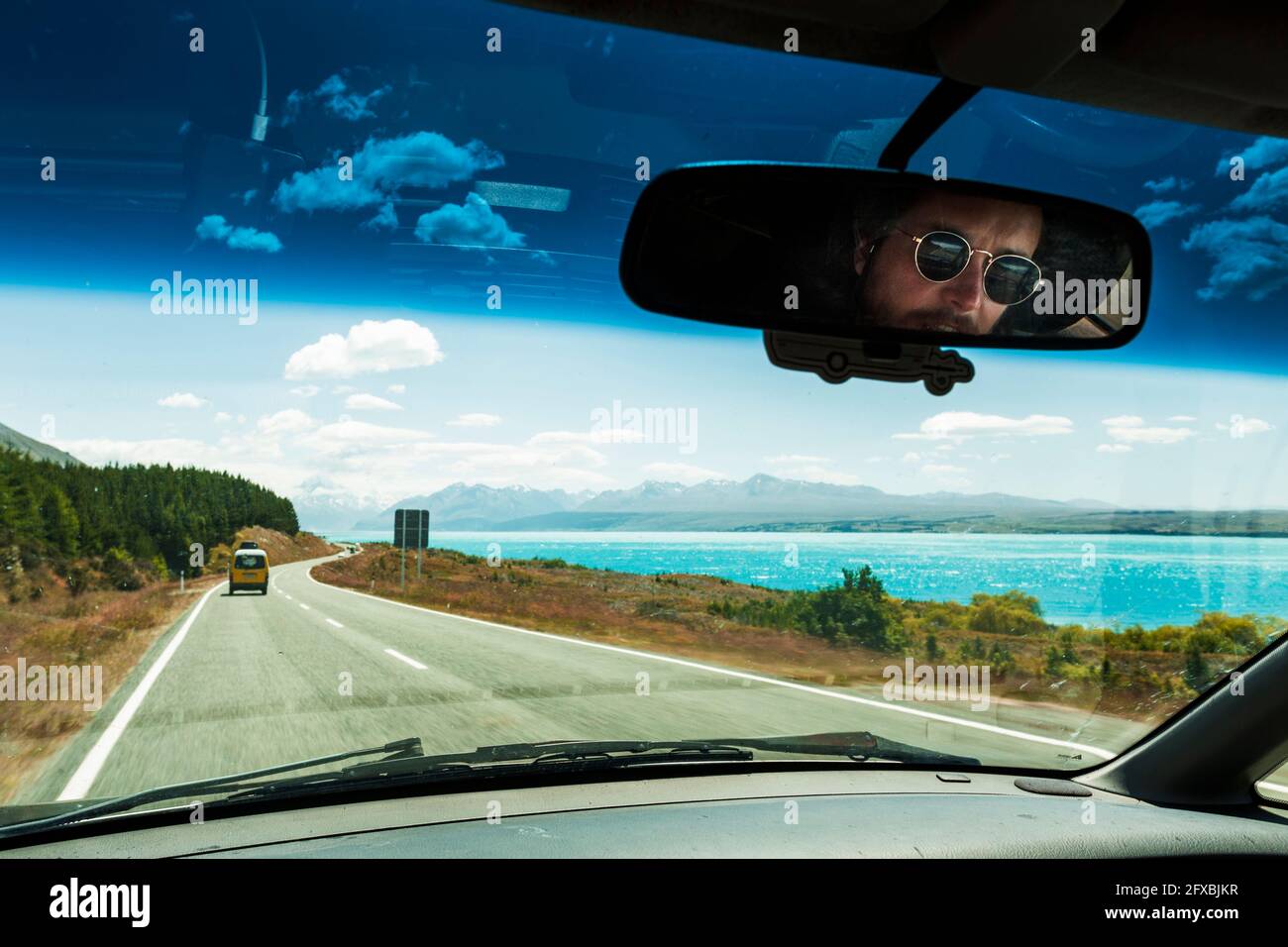 Miroir de vision arrière reflet de l'homme conduisant une voiture le long du lac sur l'autoroute Banque D'Images