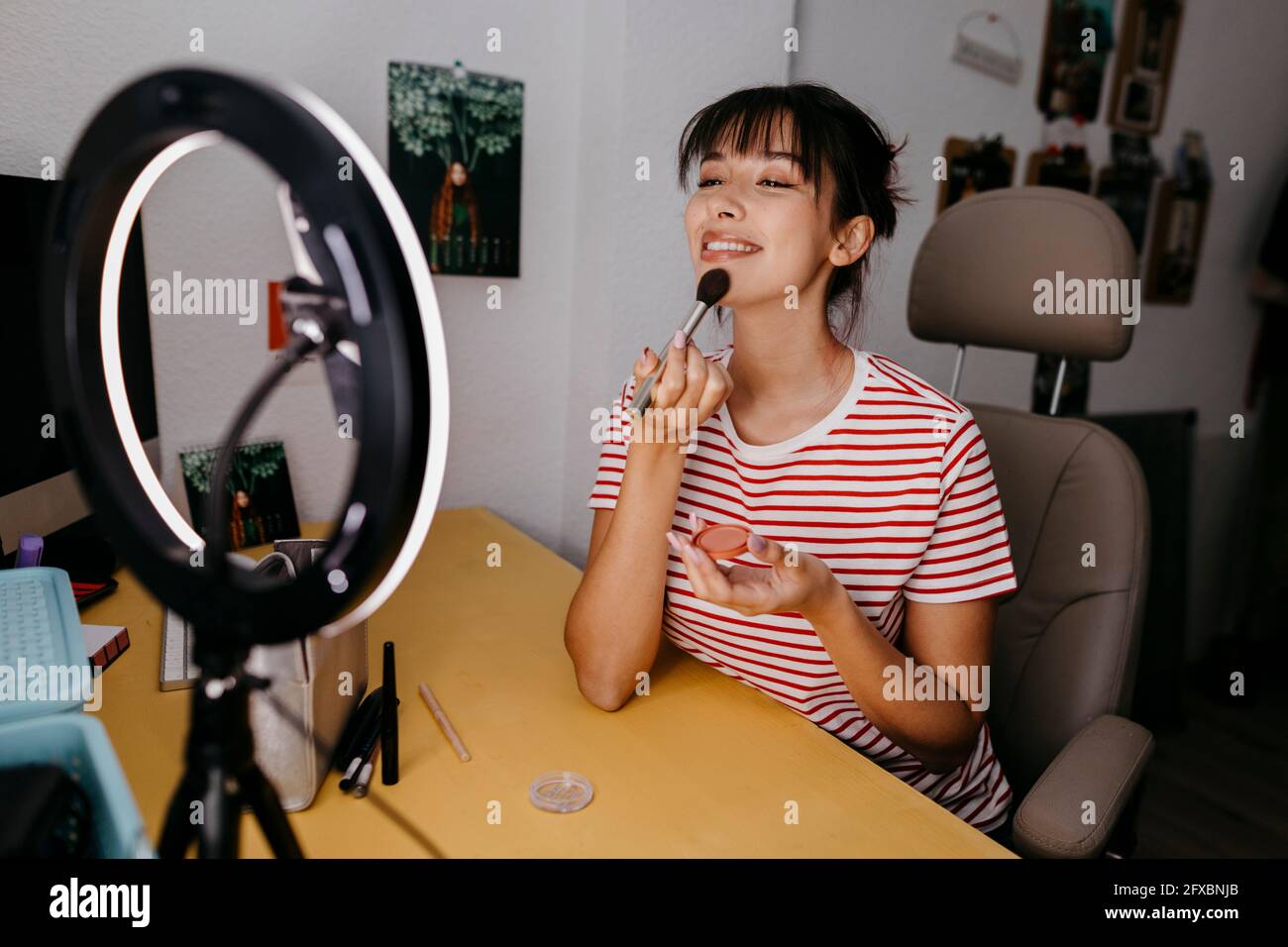Influenceur féminin utilisant un téléphone mobile tout en se vantant du maquillage en studio Banque D'Images