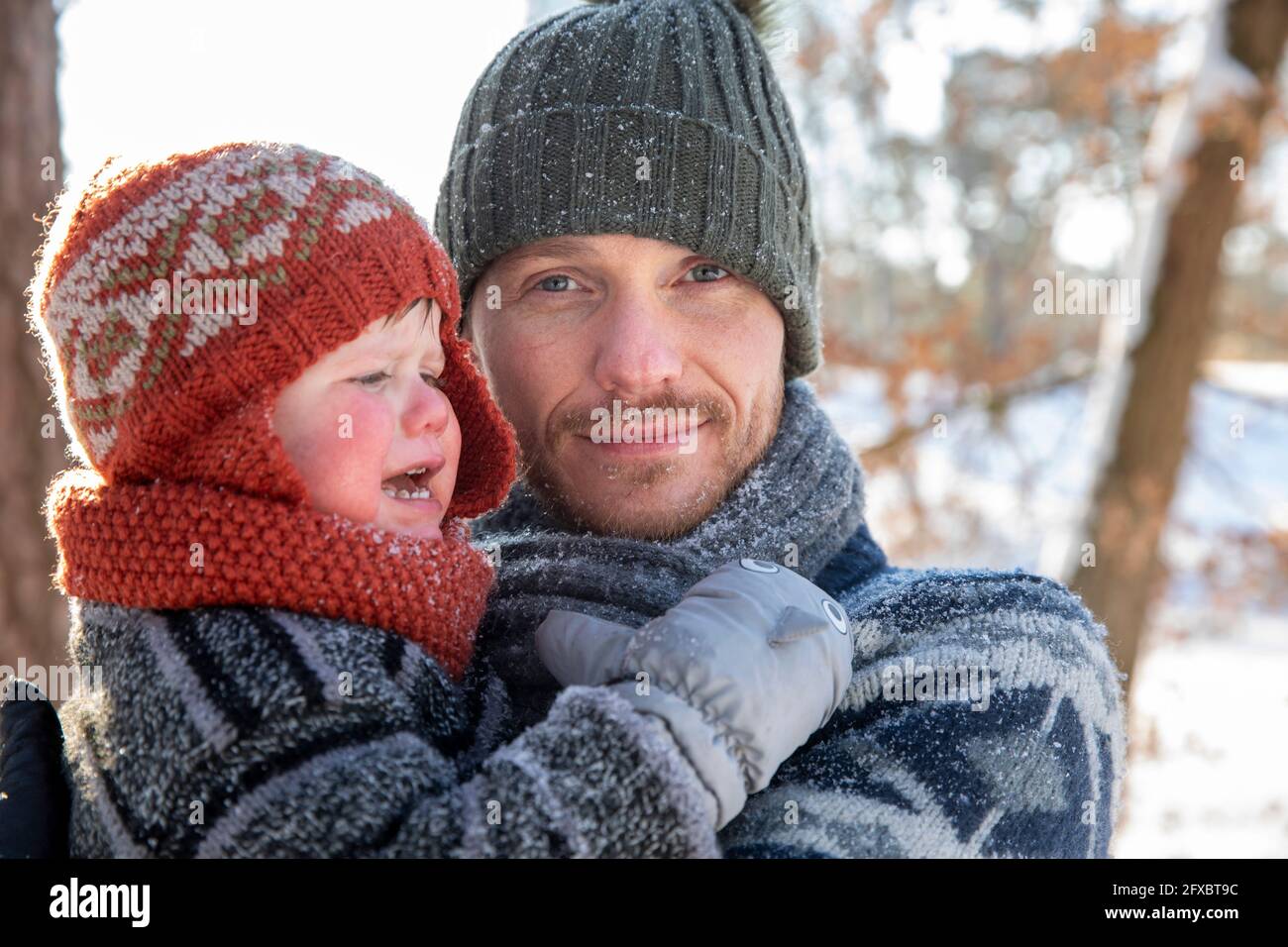 Père avec chapeau en tricot tenant le fils en pleurs pendant l'hiver Banque D'Images