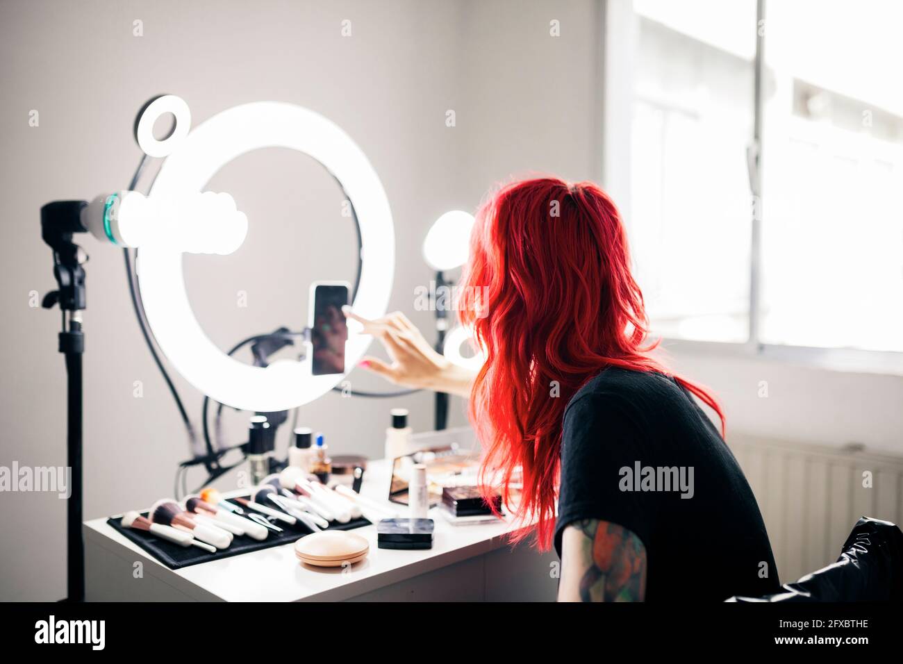 Artiste féminine aux cheveux rouges teints utilisant un smartphone tout en se vouvrant au studio Banque D'Images