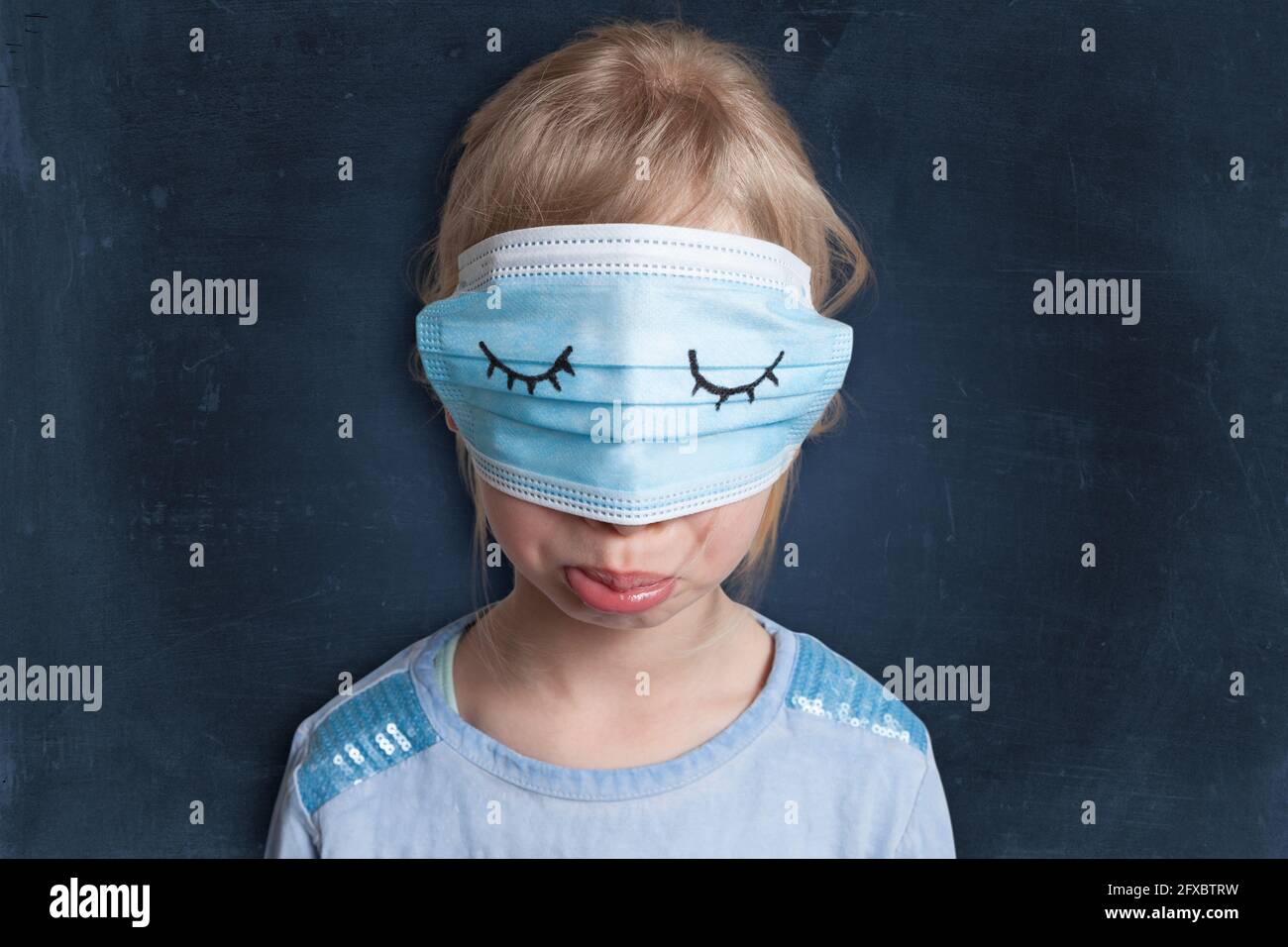Mécontent fille de porter un masque sur les yeux contre fond noir Banque D'Images