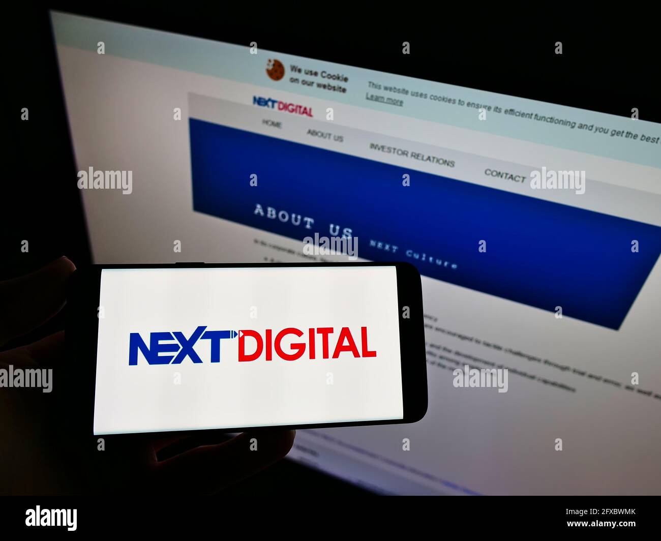 Personne tenant un téléphone portable avec le logo de la société de médias de Hong Kong Next Digital Limited à l'écran en face de la page Web. Mise au point sur l'affichage du téléphone. Banque D'Images