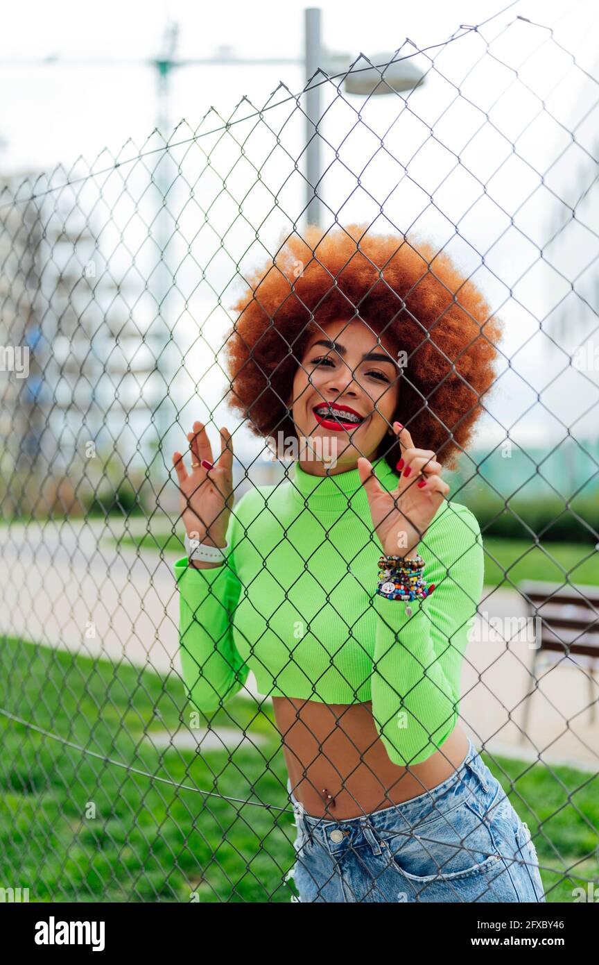 Femme à tête rousse sur une clôture penchée dans un parc public Banque D'Images Femme à tête rousse sur une clôture penchée dans un parc public Banque D'Images