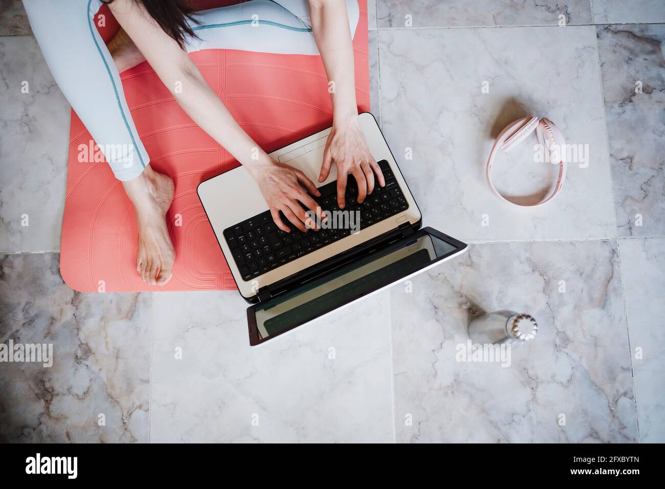 Athlète féminine utilisant un ordinateur portable assis sur un tapis d'exercice à la maison Banque D'Images
