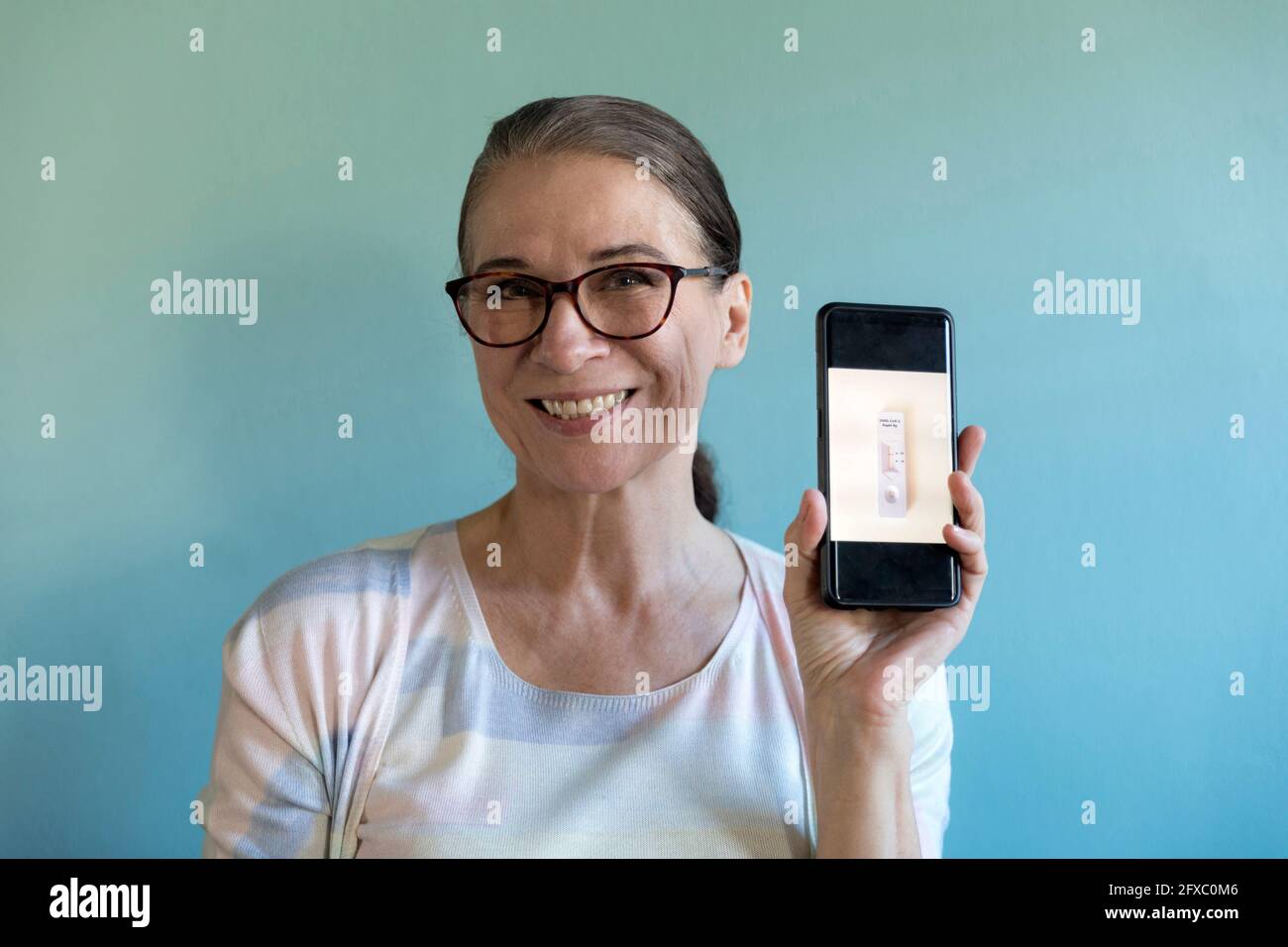 Femme souriante tenant COVID-19 test rapide contre le mur Banque D'Images