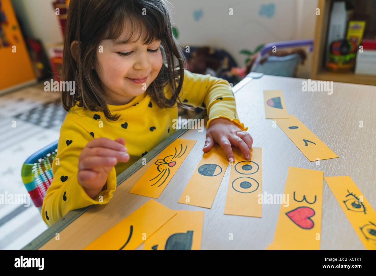 Jolie fille jouant avec des smileys sur la table dans la salle de jeux à la maison Banque D'Images Jolie fille jouant avec des smileys sur la table dans la salle de jeux à la maison Banque D'Images