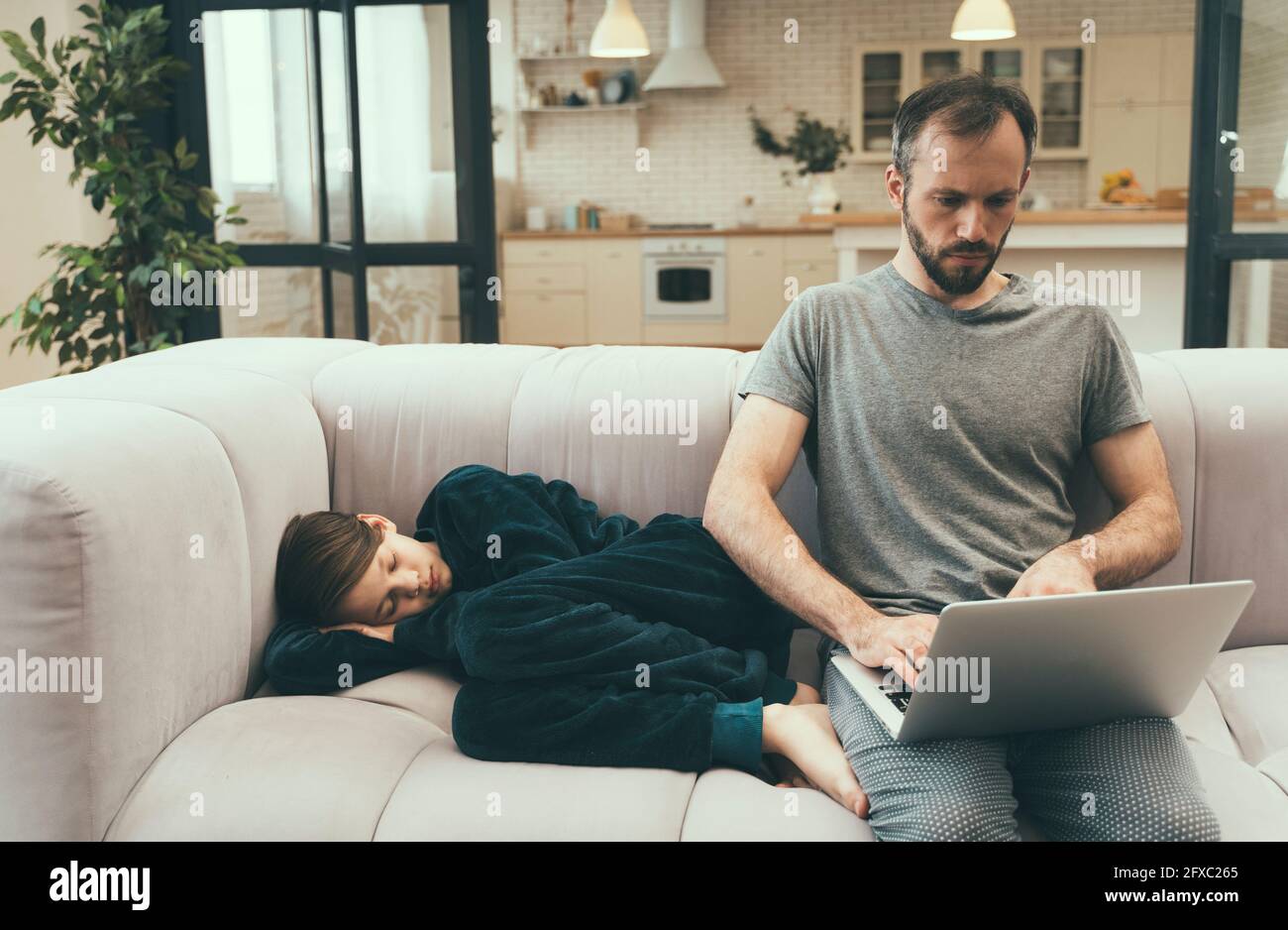 Un fils dormant à côté de son père à l'aide d'un ordinateur portable sur un canapé à la maison Banque D'Images