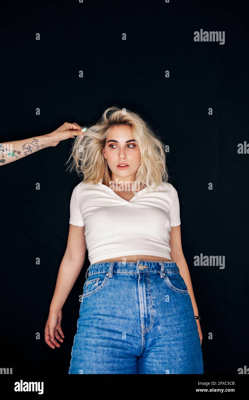 Mannequin blonde regardant la main du coiffeur sur fond noir Banque D'Images