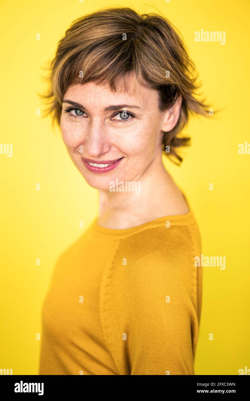 Femme mûre regardant tout en souriant sur fond jaune Banque D'Images