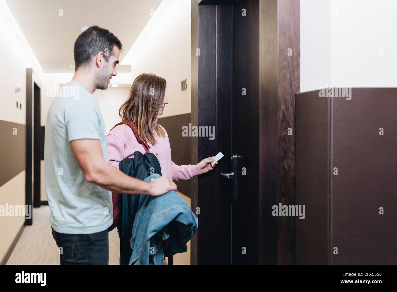Femme utilisant la clé de la carte pour déverrouiller la porte en se tenant debout près de l'homme à l'hôtel Banque D'Images