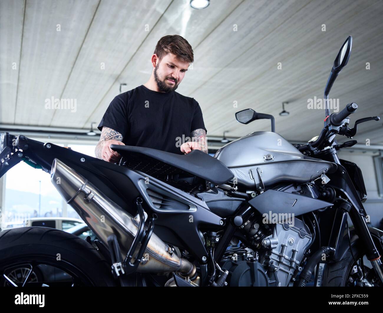 Jeune homme réparateur installant une pièce de moto au garage Banque D'Images