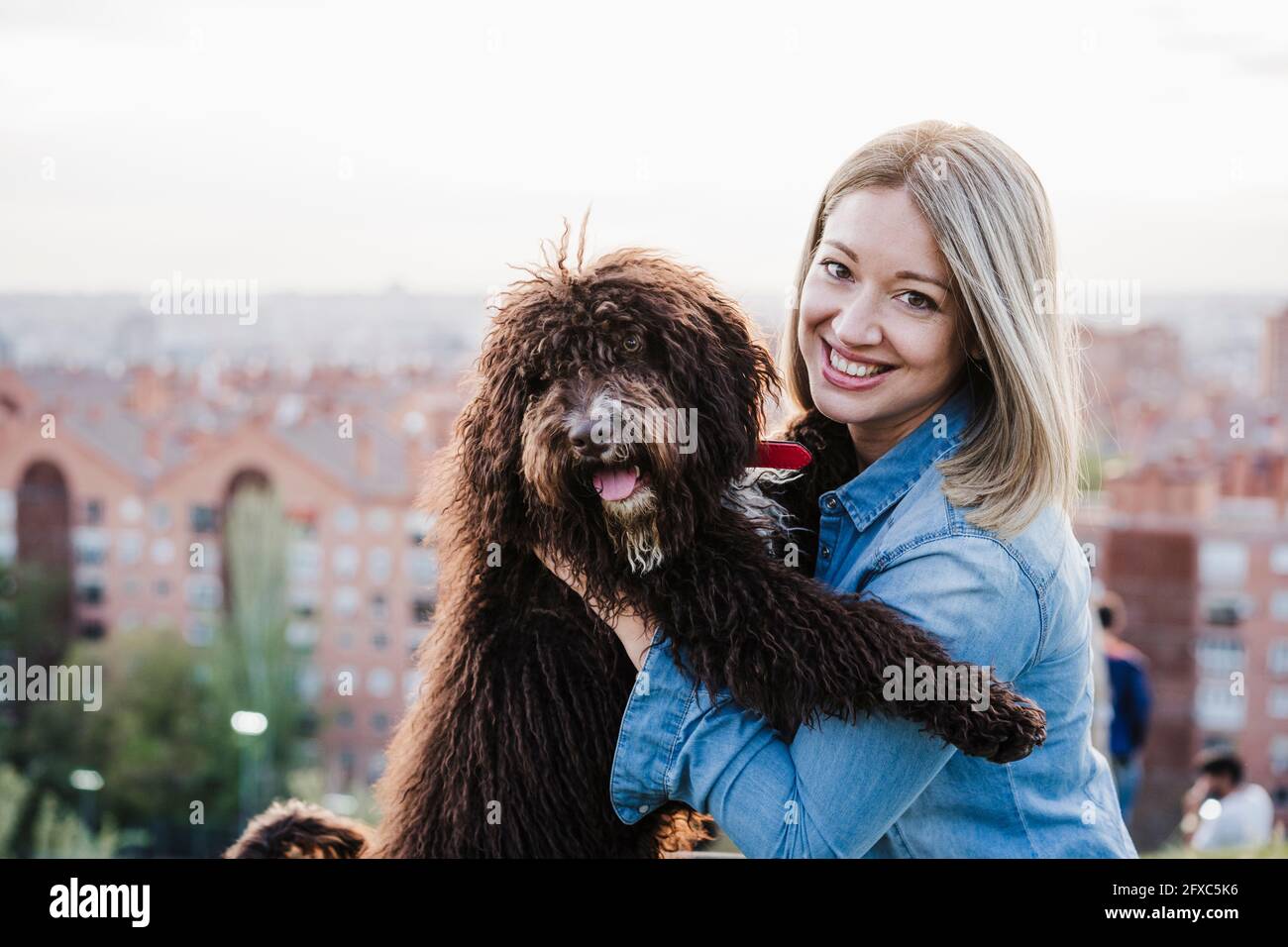 Femme mi-adulte souriante transportant un chien par paysage urbain Banque D'Images