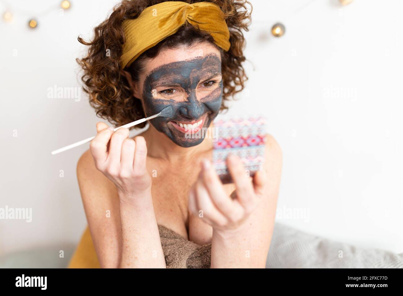 Femme gaie appliquant un masque dans la chambre à la maison Banque D'Images