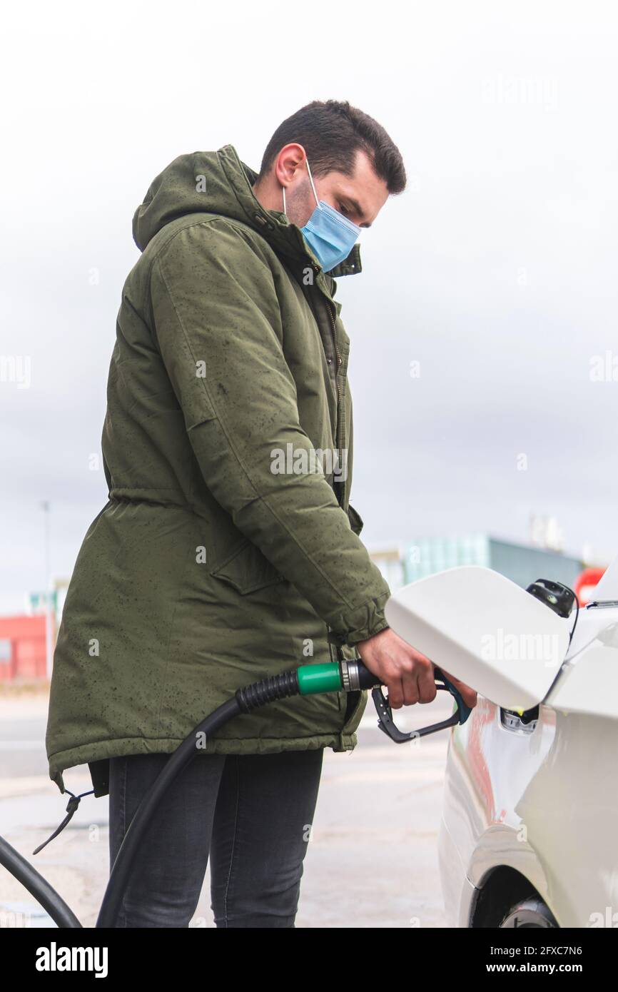 Homme avec masque facial de protection ravitailleur de voiture à la station-service pendant COVID-19 Banque D'Images