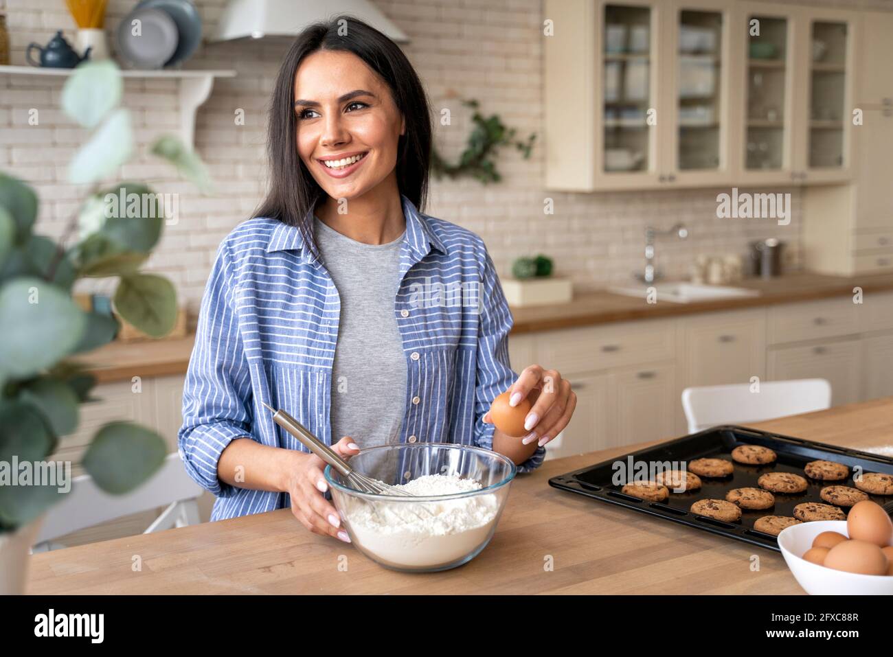 Femme souriante regardant loin de tenir l'oeuf tout en préparant la nourriture dans la cuisine à la maison Banque D'Images