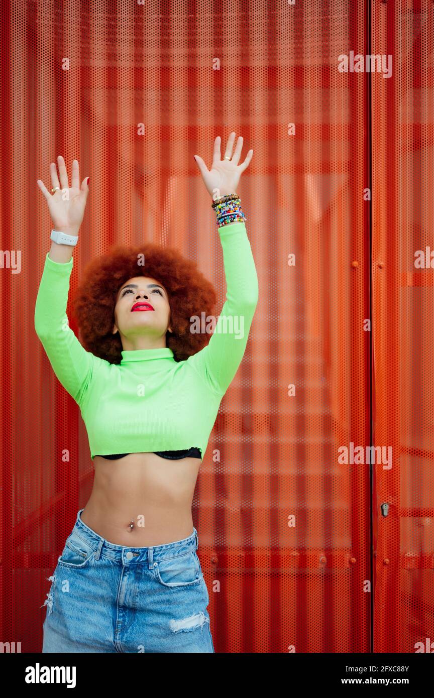 Femme afro avec les bras levés debout devant un mur en métal Banque D'Images Femme afro avec les bras levés debout devant un mur en métal Banque D'Images