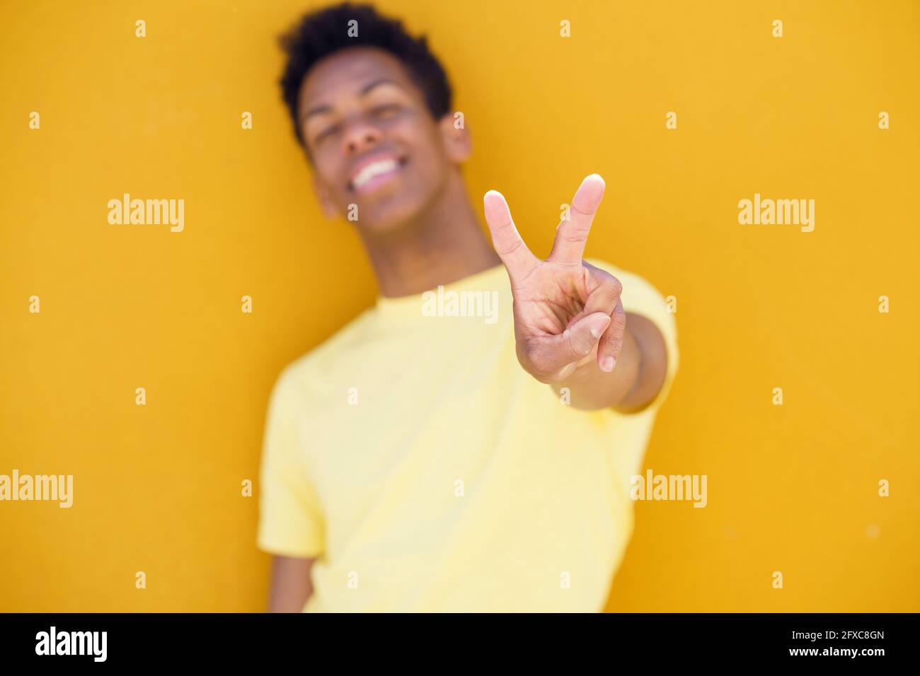 Homme souriant montrant le geste de paix devant le mur jaune Banque D'Images