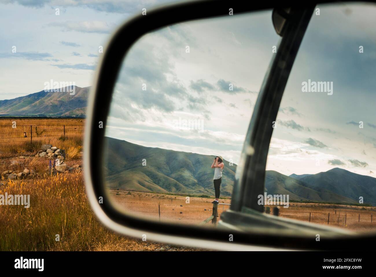Miroir à vue latérale reflet d'un jeune homme se tenant au-dessus de la clôture et regardant à travers des jumelles les montagnes environnantes Banque D'Images