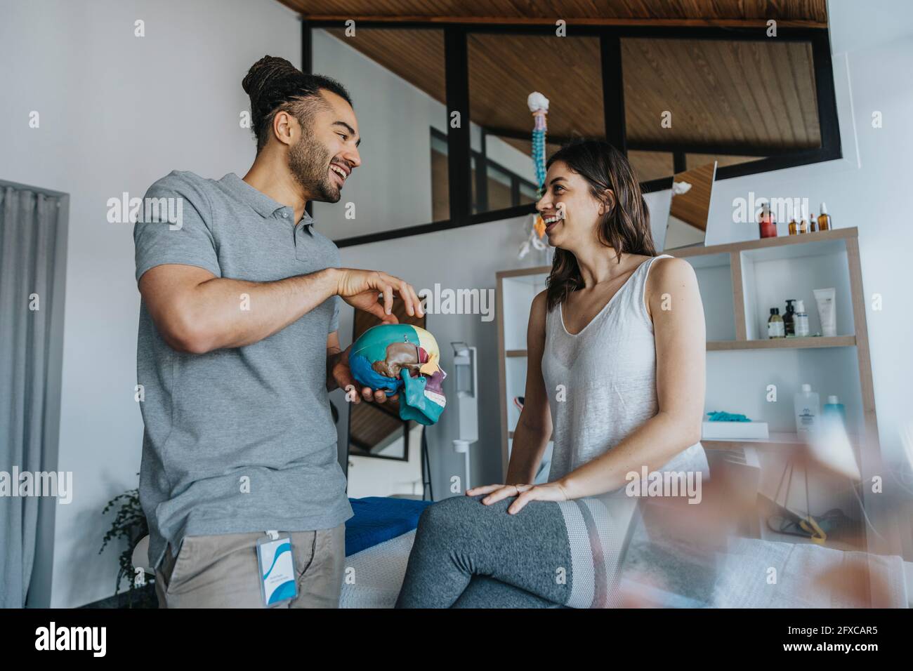 Thérapeute physique masculin souriant expliquant le modèle du crâne à la patiente en pratique Banque D'Images
