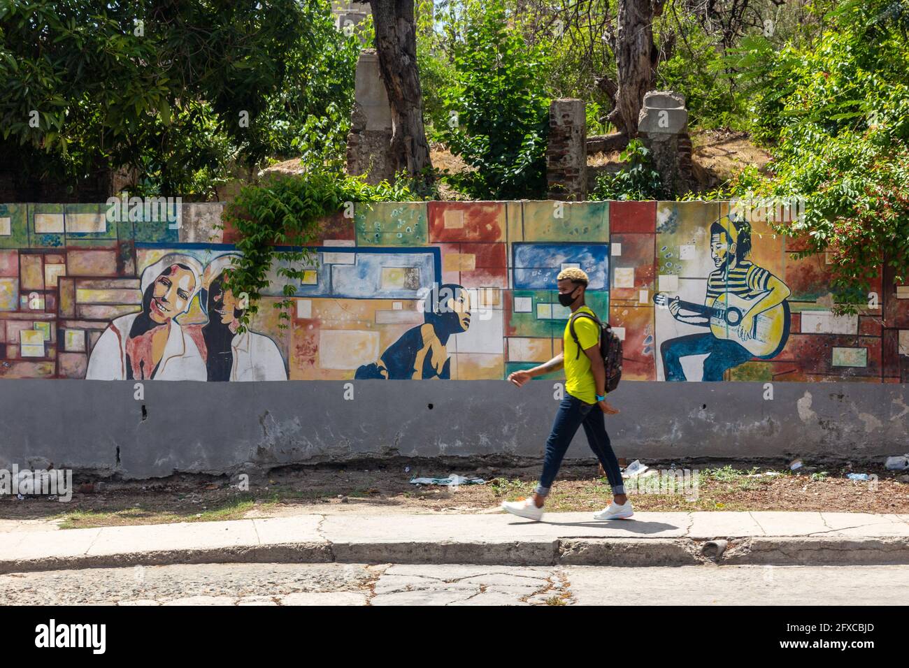 Fresque d'art urbain sur l'Avenida Trocha à Santiago de Cuba, Cuba. Un jeune Afro Caribbean marche avec un masque protecteur. Banque D'Images