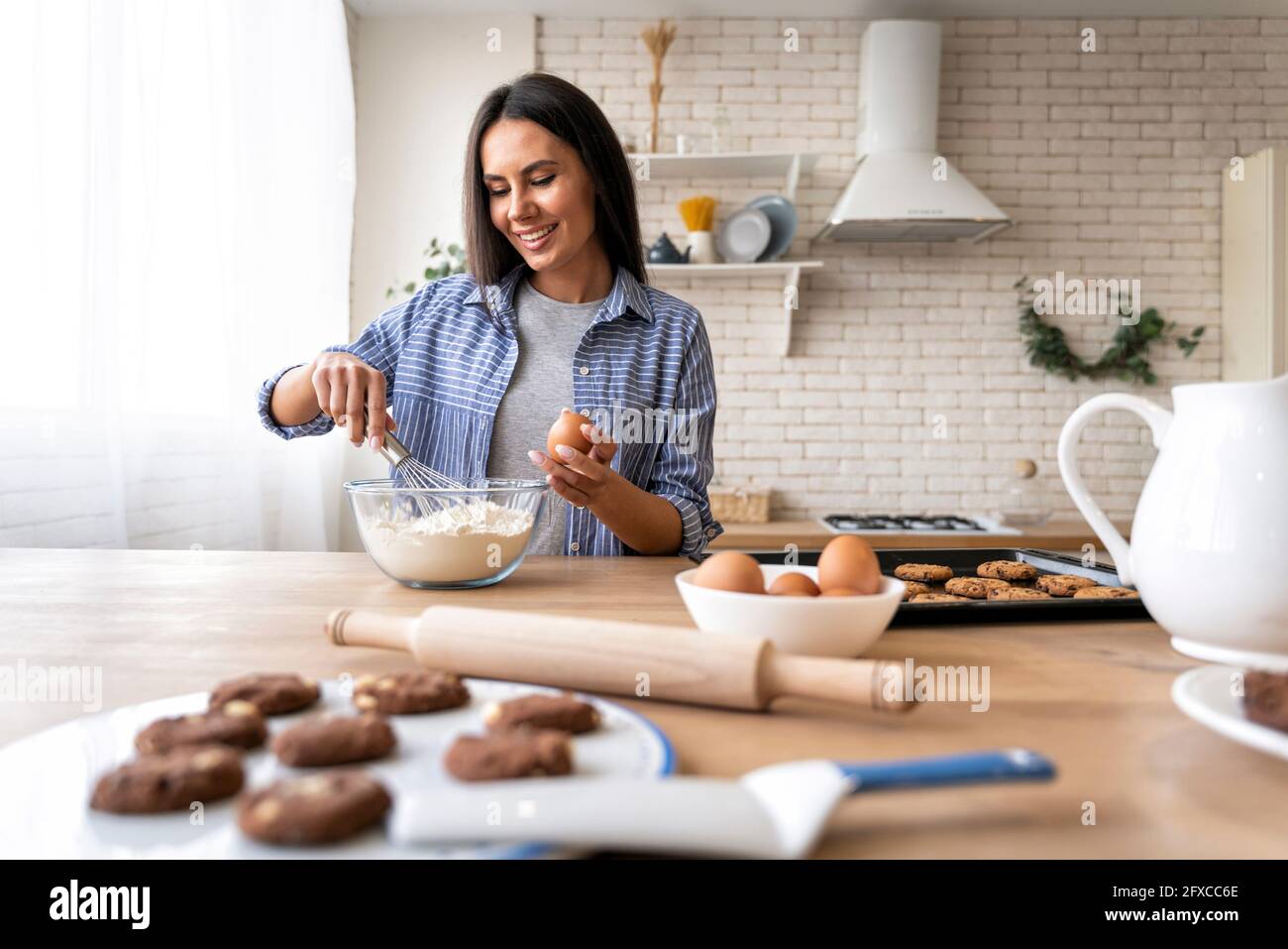 Femme mélangeant la farine tout en tenant l'oeuf dans la cuisine Banque D'Images