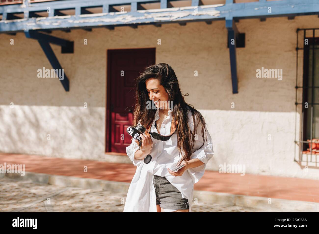 Femme souriant tout en tenant la caméra au village pendant la journée ensoleillée Banque D'Images