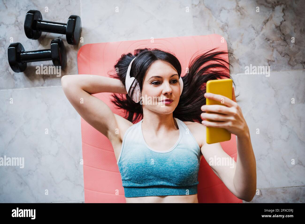 Femme utilisant un smartphone tout en se relaxant sur un tapis d'exercice à la maison Banque D'Images