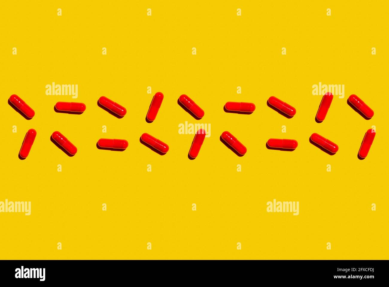 Deux rangées de capsules de médicaments rouges posées sur fond jaune Banque D'Images