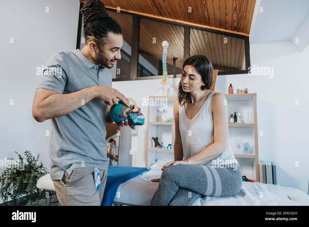 Physiothérapeute masculin expliquant le modèle du crâne à la patiente en pratique Banque D'Images