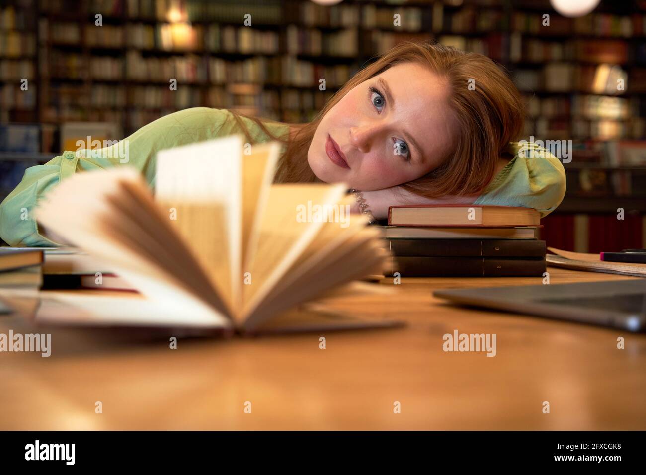 Femme regardant tout en se relaxant à table dans la bibliothèque Banque D'Images