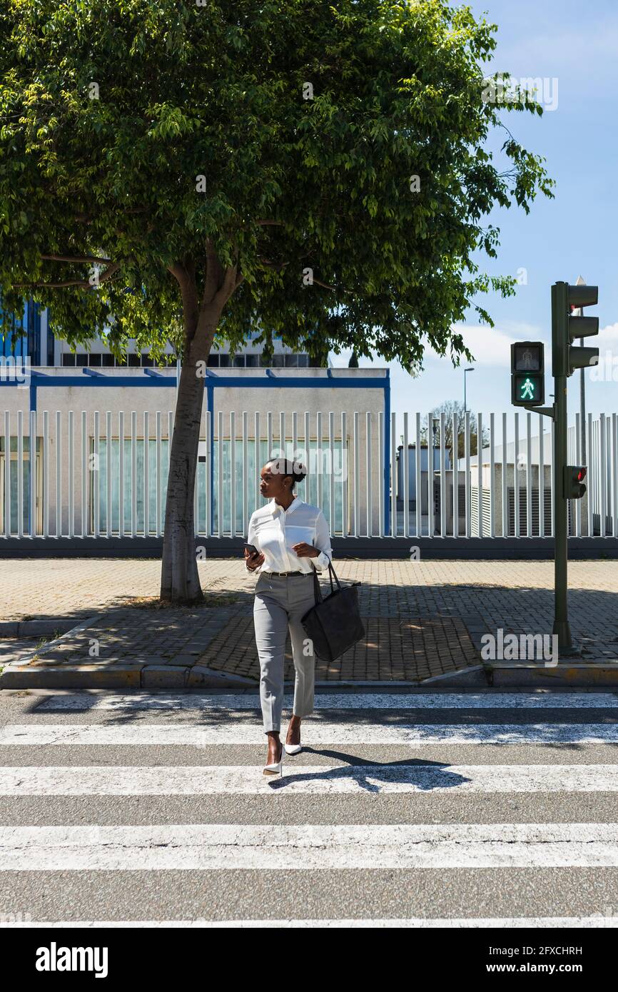 Femme entrepreneur traversant la route le jour ensoleillé Banque D'Images