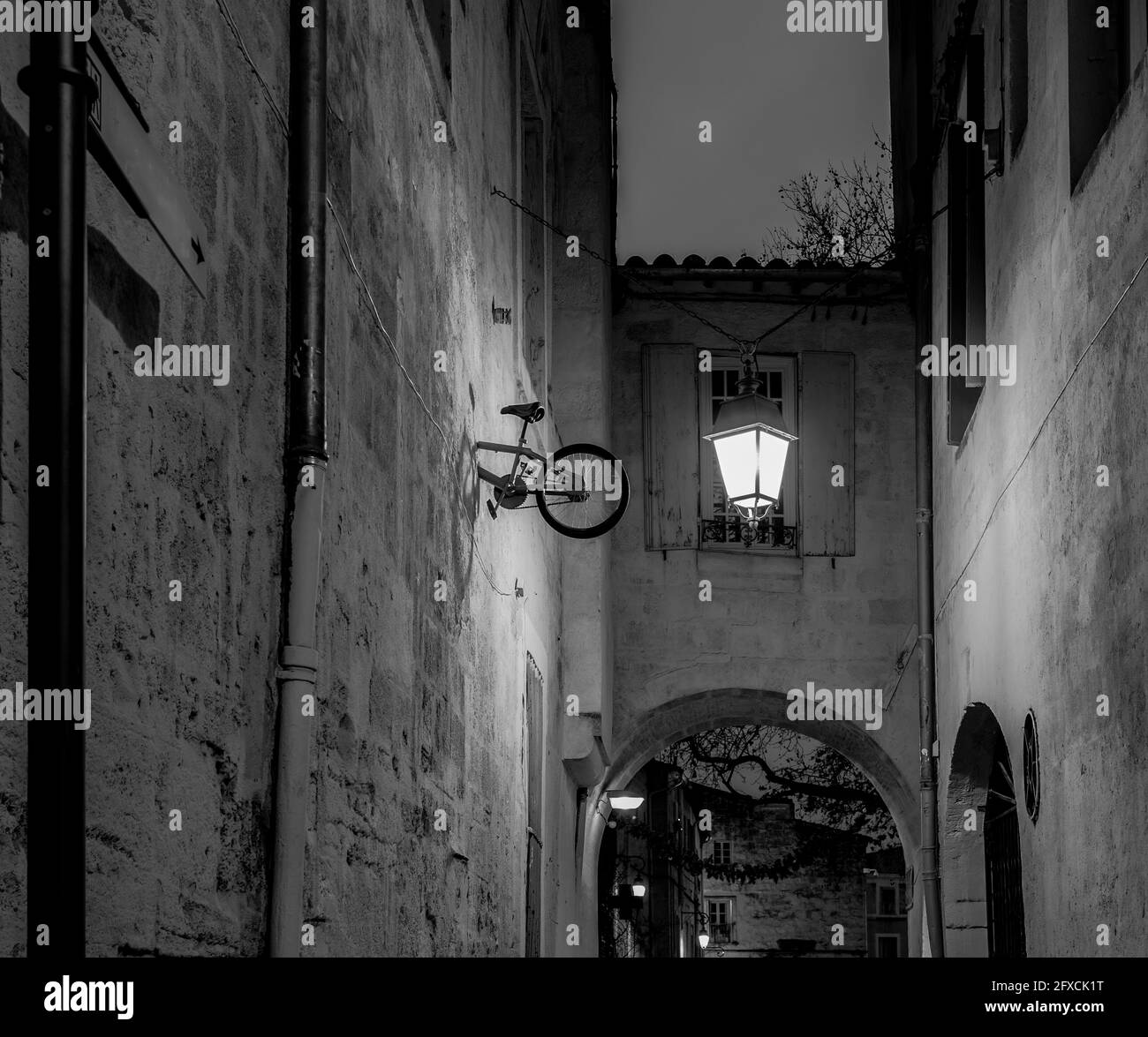 Allée étroite traditionnelle de nuit dans une vieille ville européenne avec une lampe et une installation d'art de rue - Montpellier, sud de la France ; noir et blanc Banque D'Images
