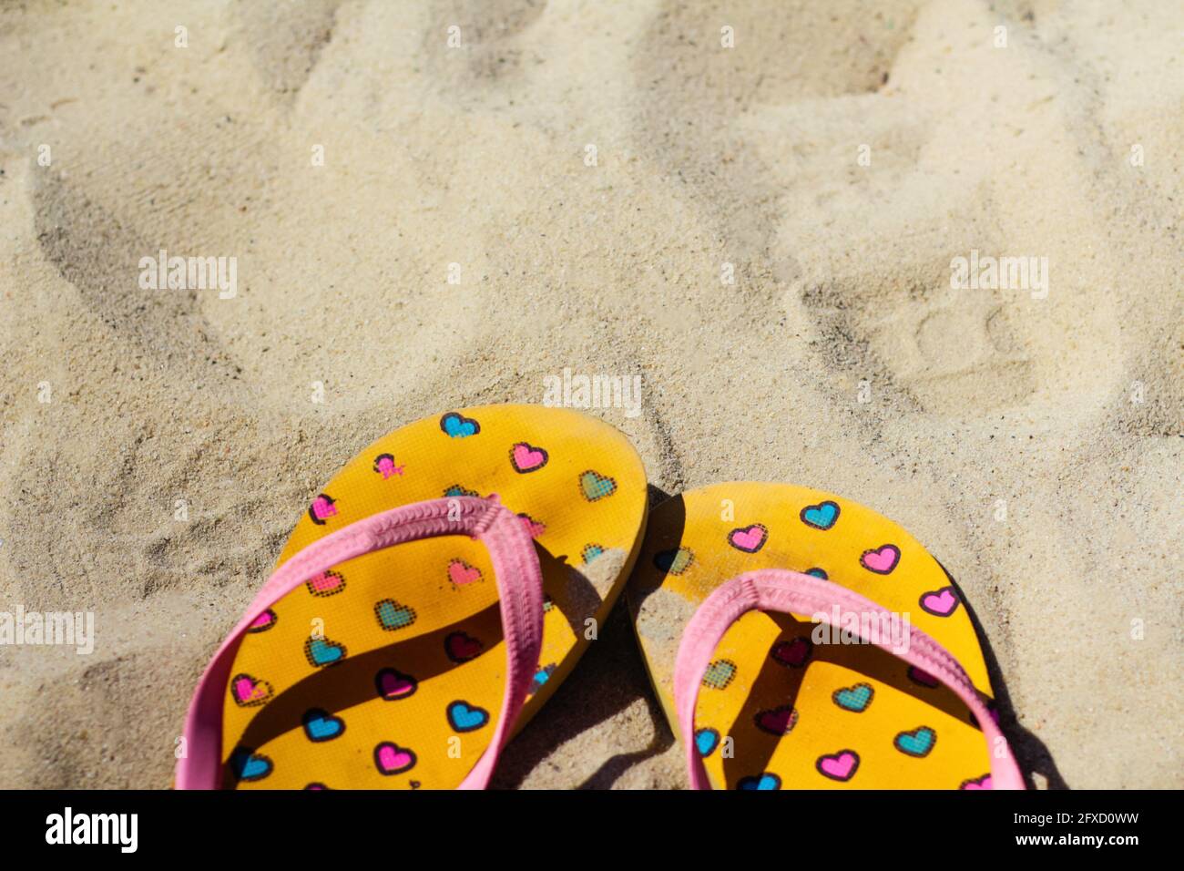 Effet de flou sale jaune vif et rose chaussons tongs avec des coeurs roses et bleus sur le sable. Arrière-plan d'été.le concept de la chaleur, de la relaxation et Banque D'Images