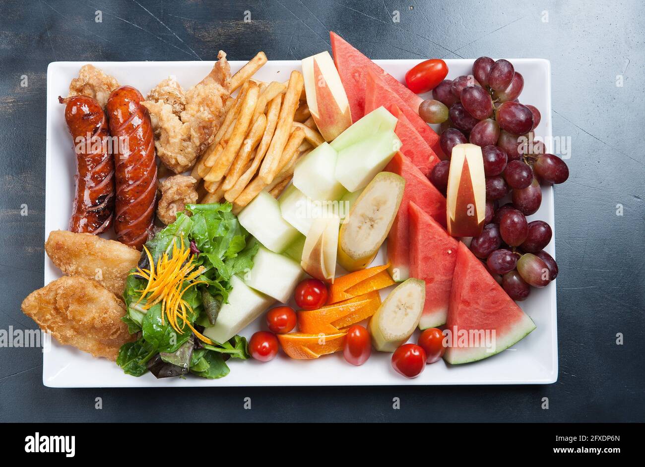 Assiette de plats asiatiques. Saucisse fumée, tempura, frites. Pastèque, raisins et salade. Banque D'Images