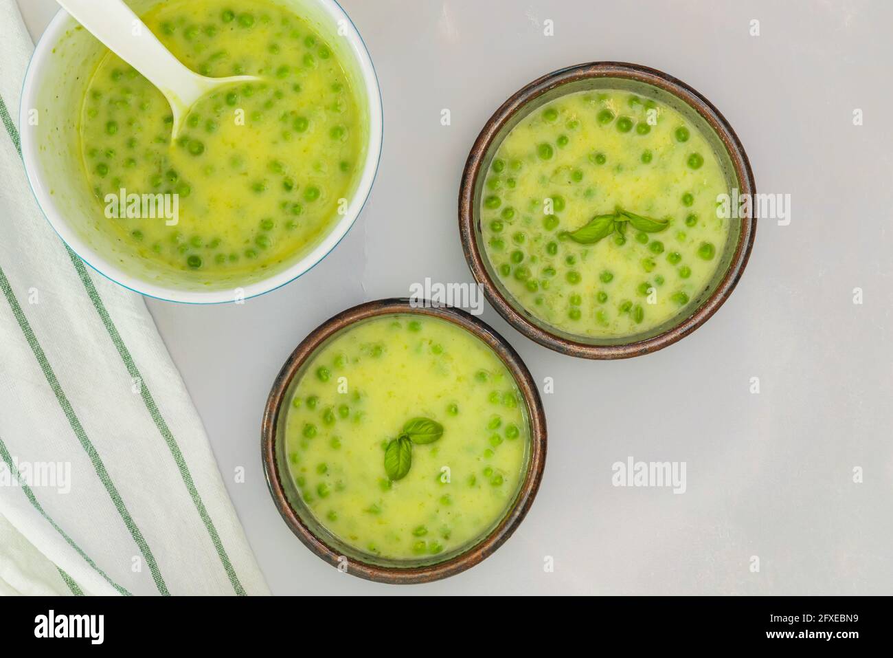 Soupe crémeuse de céleri aux petits pois verts et fond de basilclose dans des bols sur fond de marbre gris clair, vue de dessus, espace copie Banque D'Images